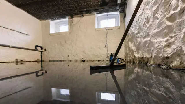 Worker squeegeeing standing water in a basement with stone walls