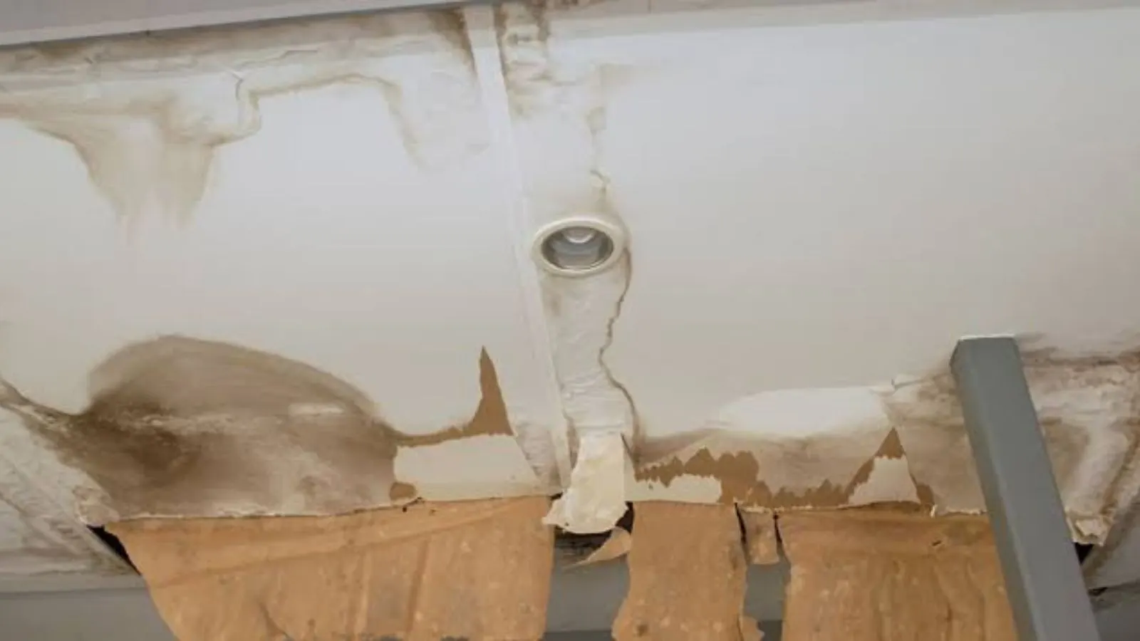 Water-stained ceiling with peeling paint and a damaged light fixture area